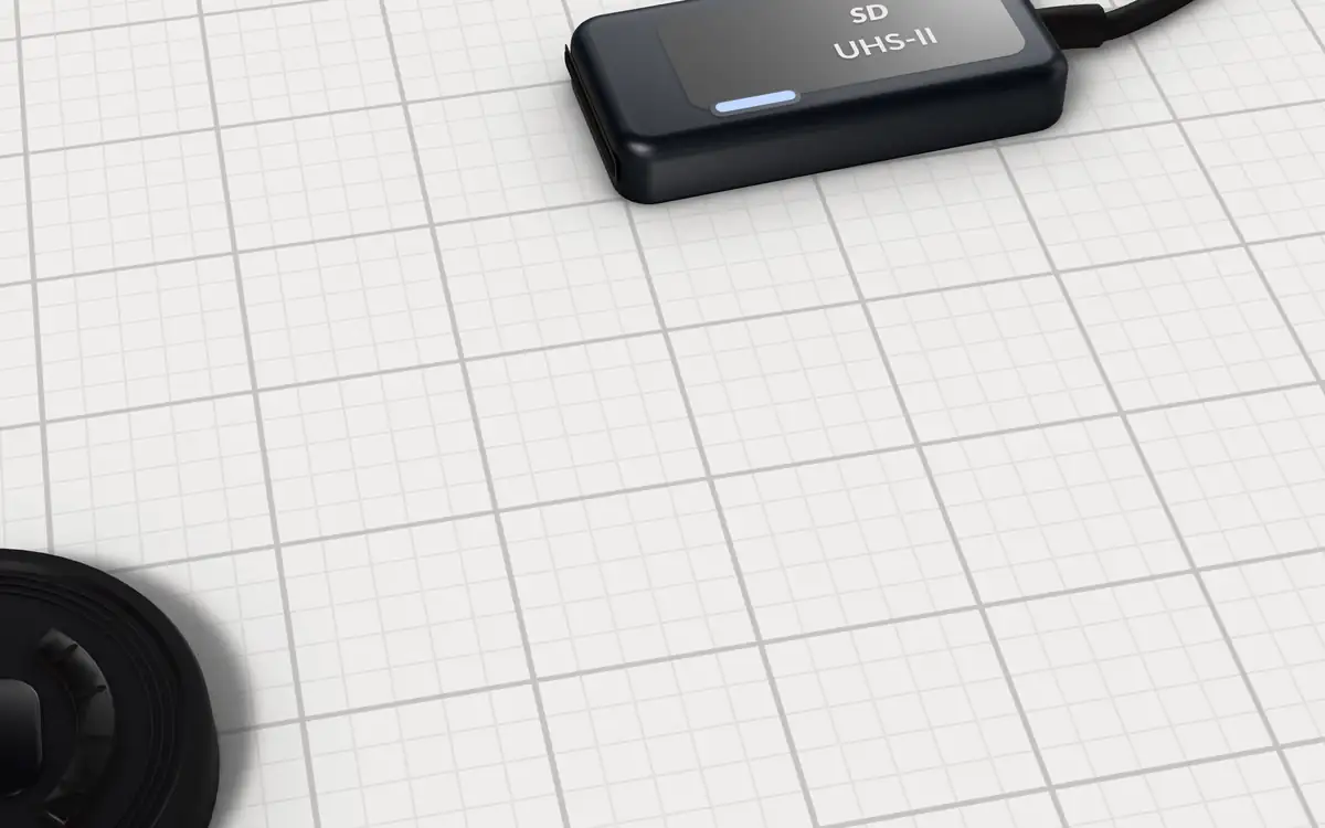 Illustration of the 5 V90 SD cards for 8K video to scale, next to a USB-C UHS-II card reader with a blinking activity light and a camera lens cap for size